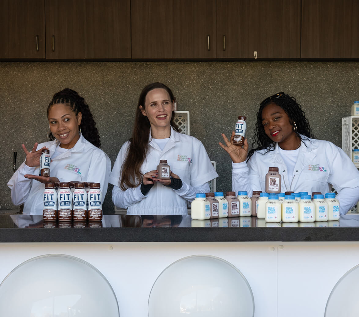 A group of Every Woman's Marathon volunteers handing out mini bottles of chocolate and white milk.