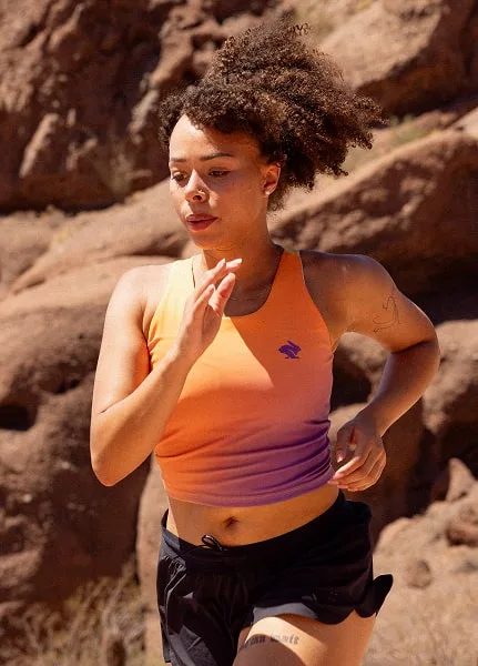 Runner wears the Every Woman's Marathon orange and purple gradient Crusher pocket crop as she runs up a hill near a rock formation.