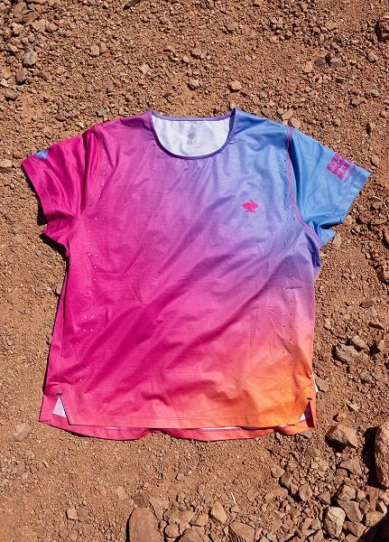 A close-up of the Every Woman's Marathon blue and pink gradient Race Pace Tee SS against desert floor.
