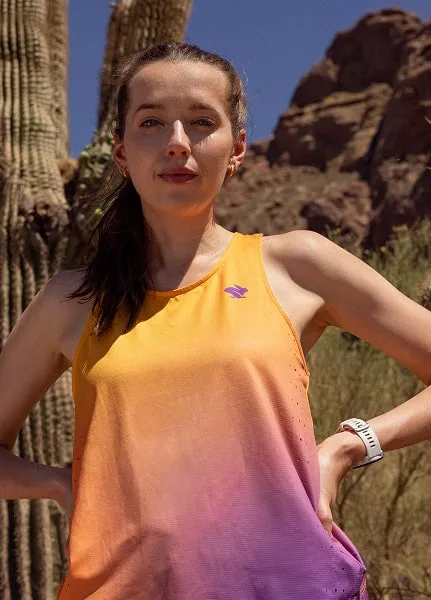 A runner wears the Every Woman's Marathon orange and purple gradient Race Pace Tank Singlet with a close up cactus behind her.