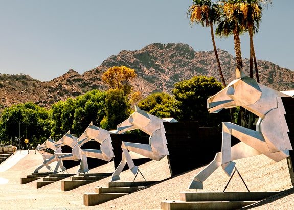 Water mark horses sculpture with mountain view and palm trees in the distance.
