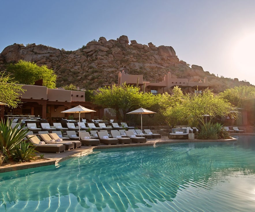 A relaxing poolside view with lounge chairs and turquoise water reflect the overhead mountains.