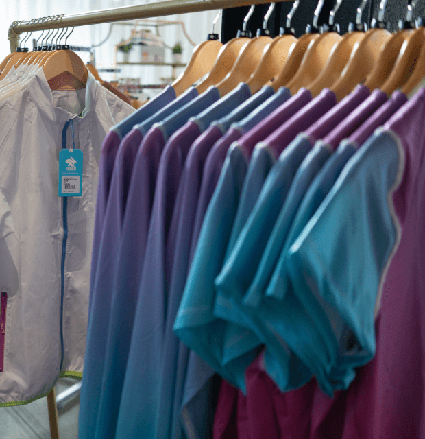 A clothing rack with white windbreakers and a gradient short sleeve and long sleeve running shirts.
