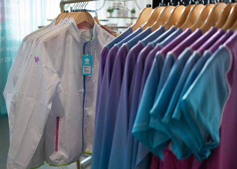 A clothing rack with white windbreakers and a gradient short sleeve and long sleeve running shirts.