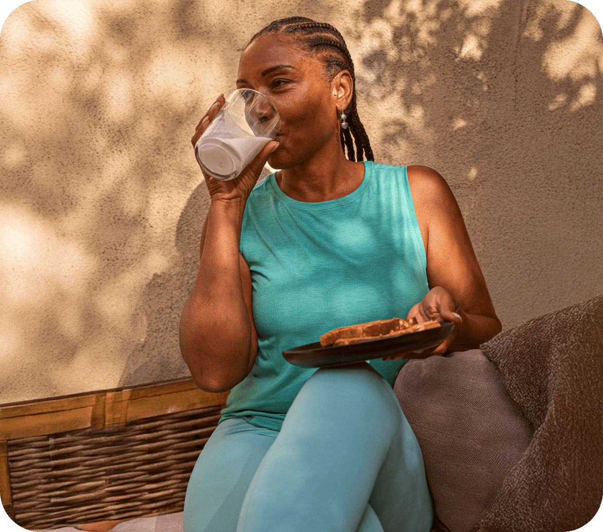 IMG_GlassofMilk A woman wearing a light blue running set standing next to a brick wall, drinking an individual size glass bottle of white milk.