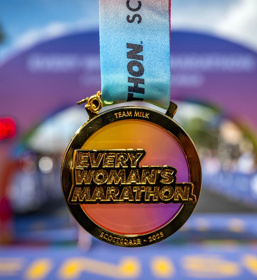 2025 Every Woman’s Marathon™ medal with the Finish Line in the background.