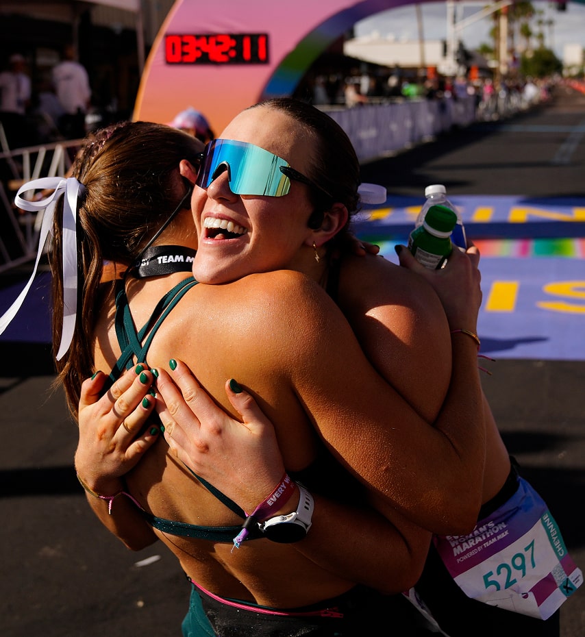Two runners embrace with happiness at the Every Woman’s Marathon finish line.