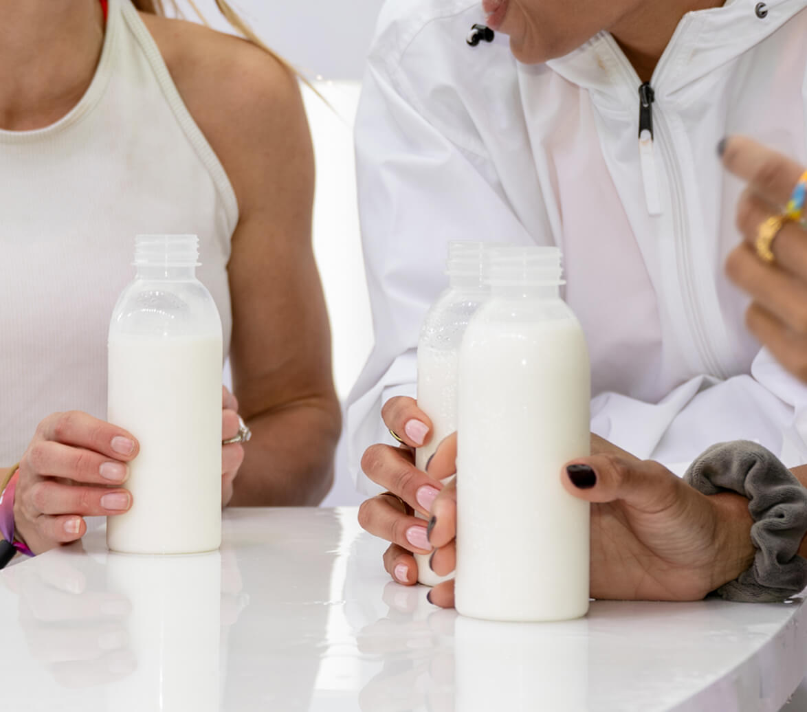 A group of women gather and drink from bottles of whole dairy milk.