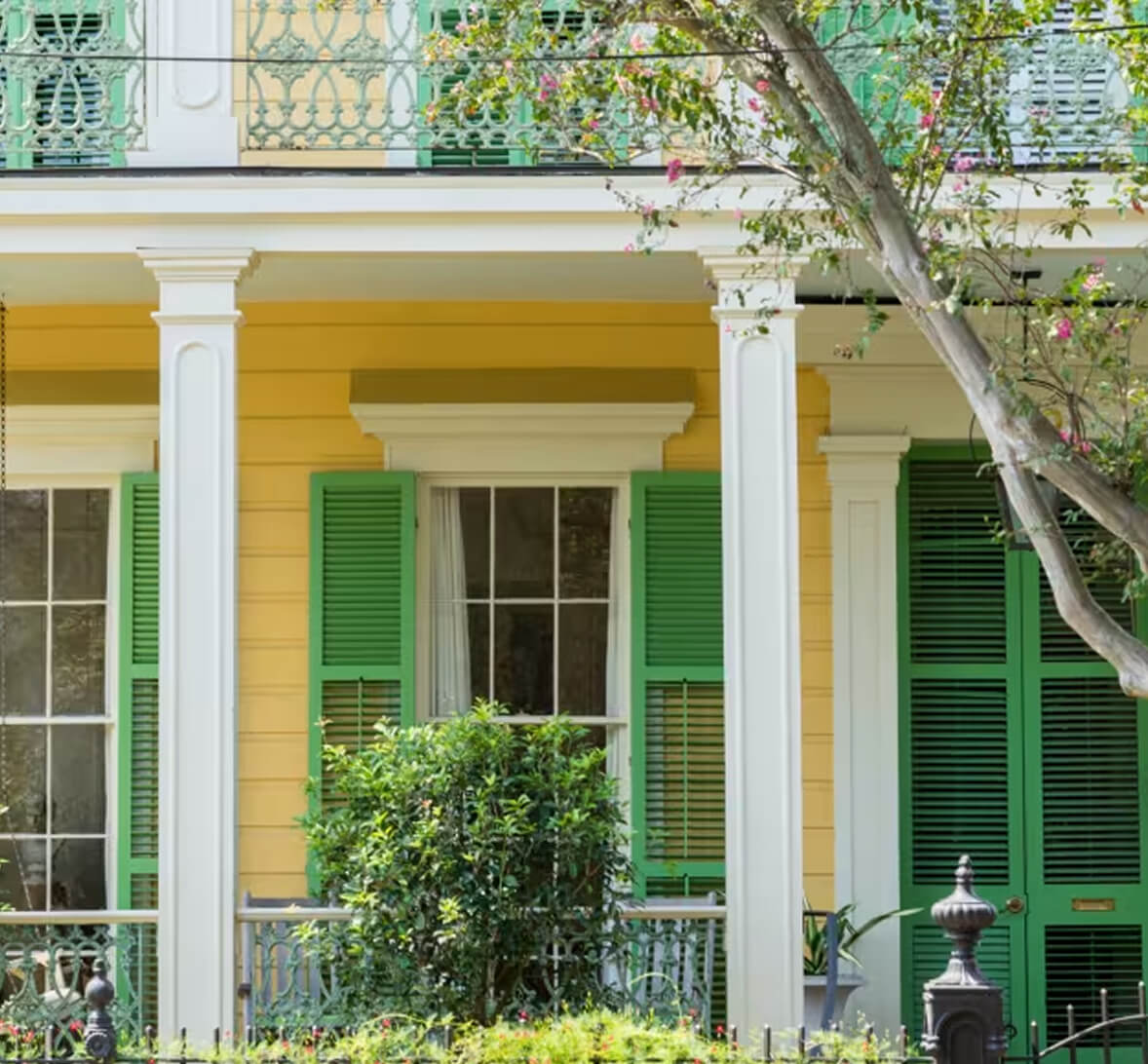 A closeup of a yellow house with white pillars and green shutters.