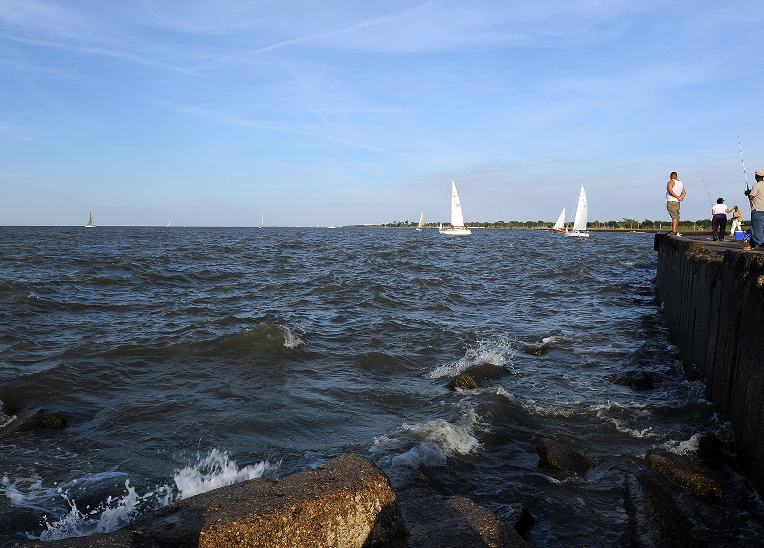 Sailboats glide along Lake Pontchartrain past a pier of onlookers.
